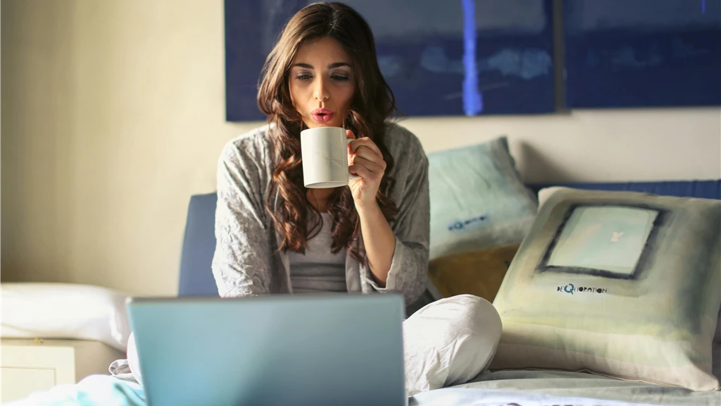 Woman in Grey Jacket Sits on Bed Uses Grey Laptop