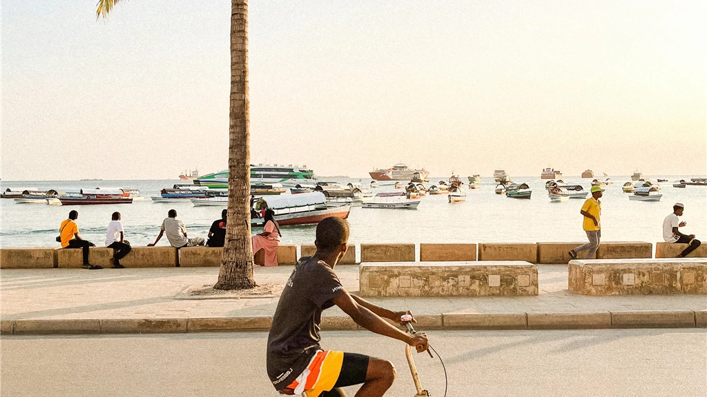 Young Man Riding a Bicycle Along the Coast Looking at the Boats Anchored by the Shore