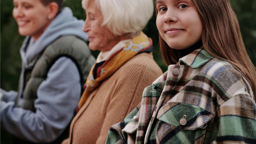 Teenage girl leaning on chair next to relatives outdoors