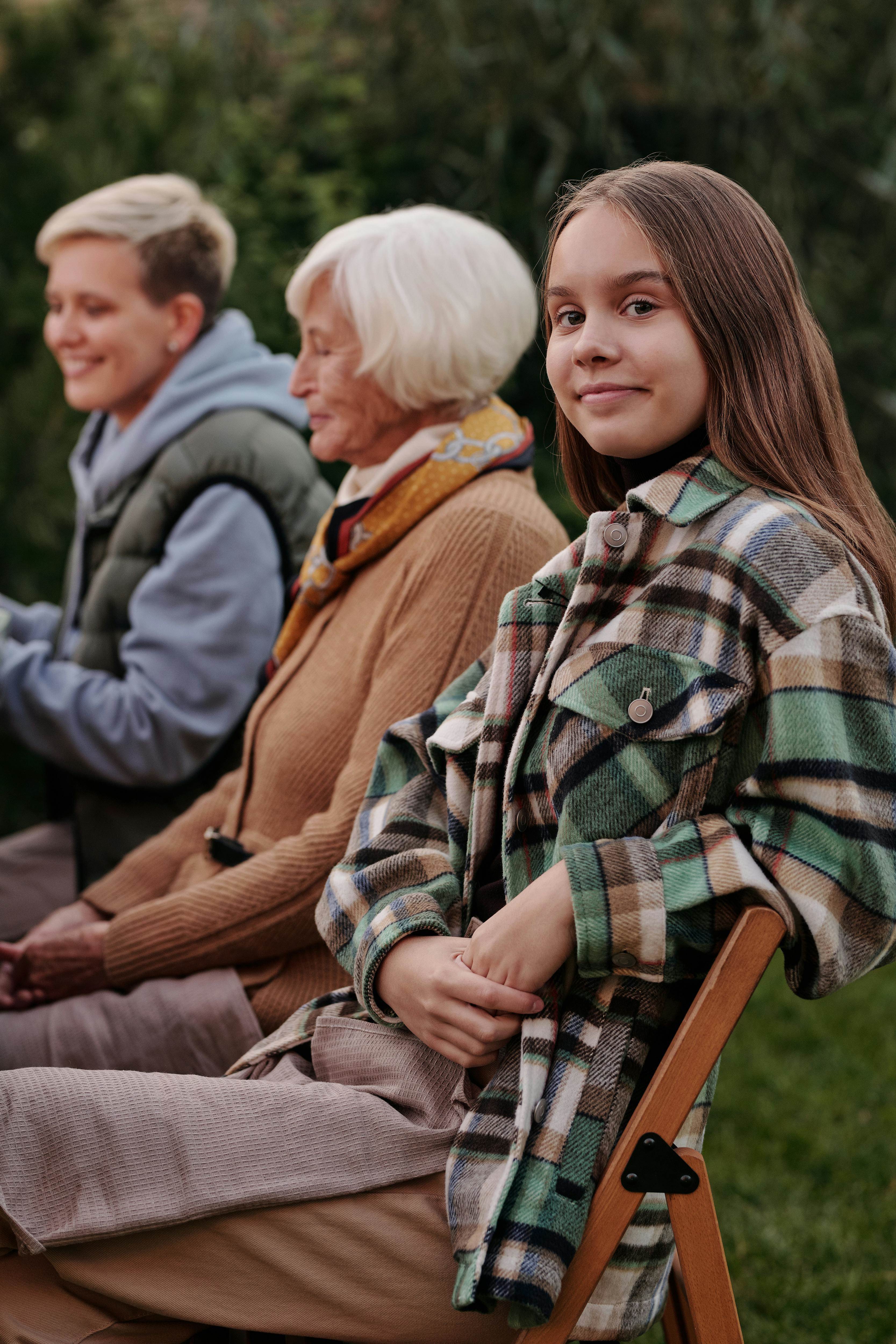 Teenage girl leaning on chair next to relatives outdoors